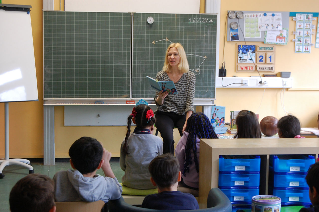 Eine Frau steht vor einer Gruppe Kinder und liest vor