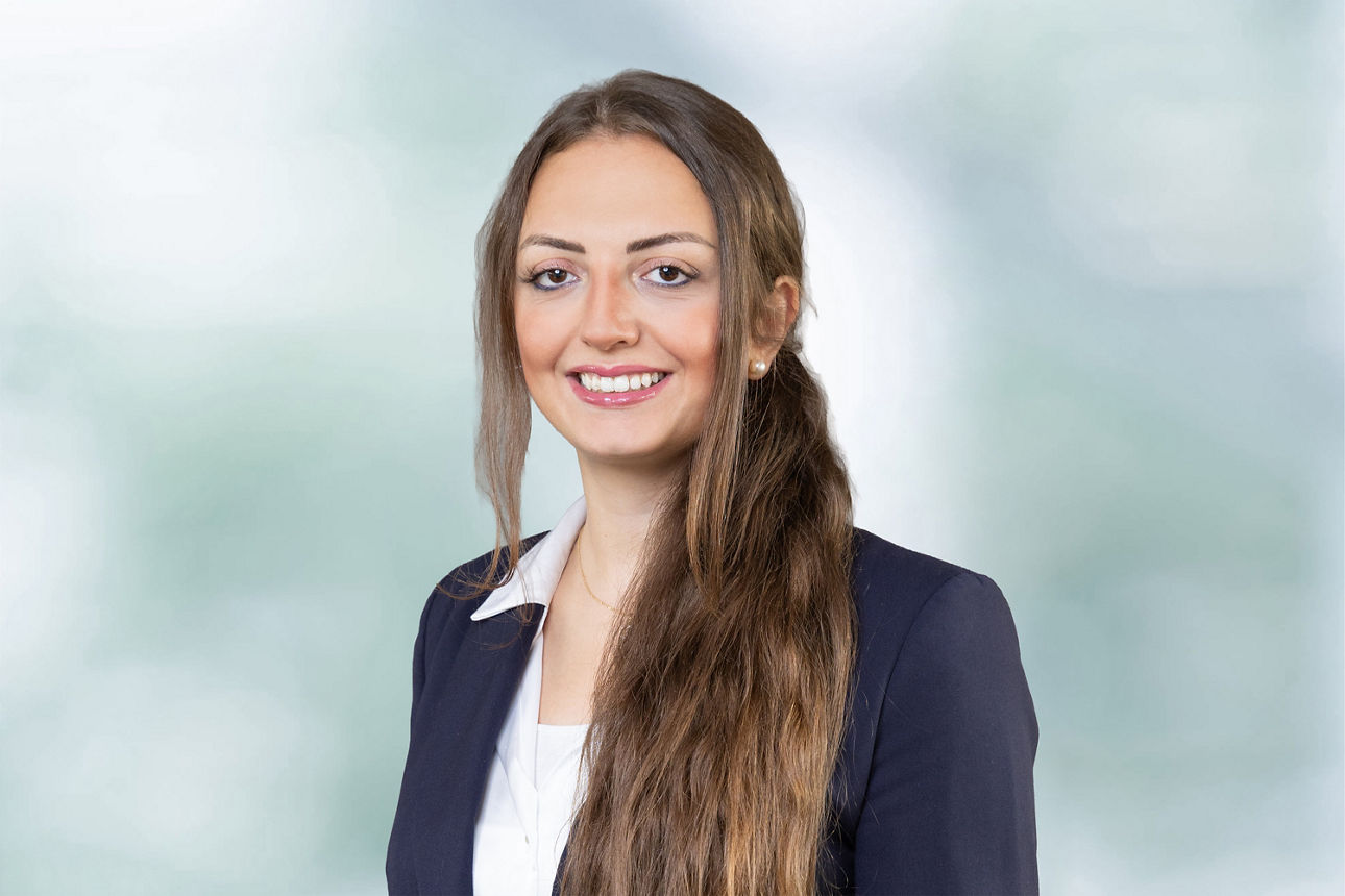 Portraitaufnahme unserer Kollegin Hedroj, Zeinab.. Sie trägt eine weiße Bluse unter einem dunkelblauen Blazer. Frau Hedroj lächelt.