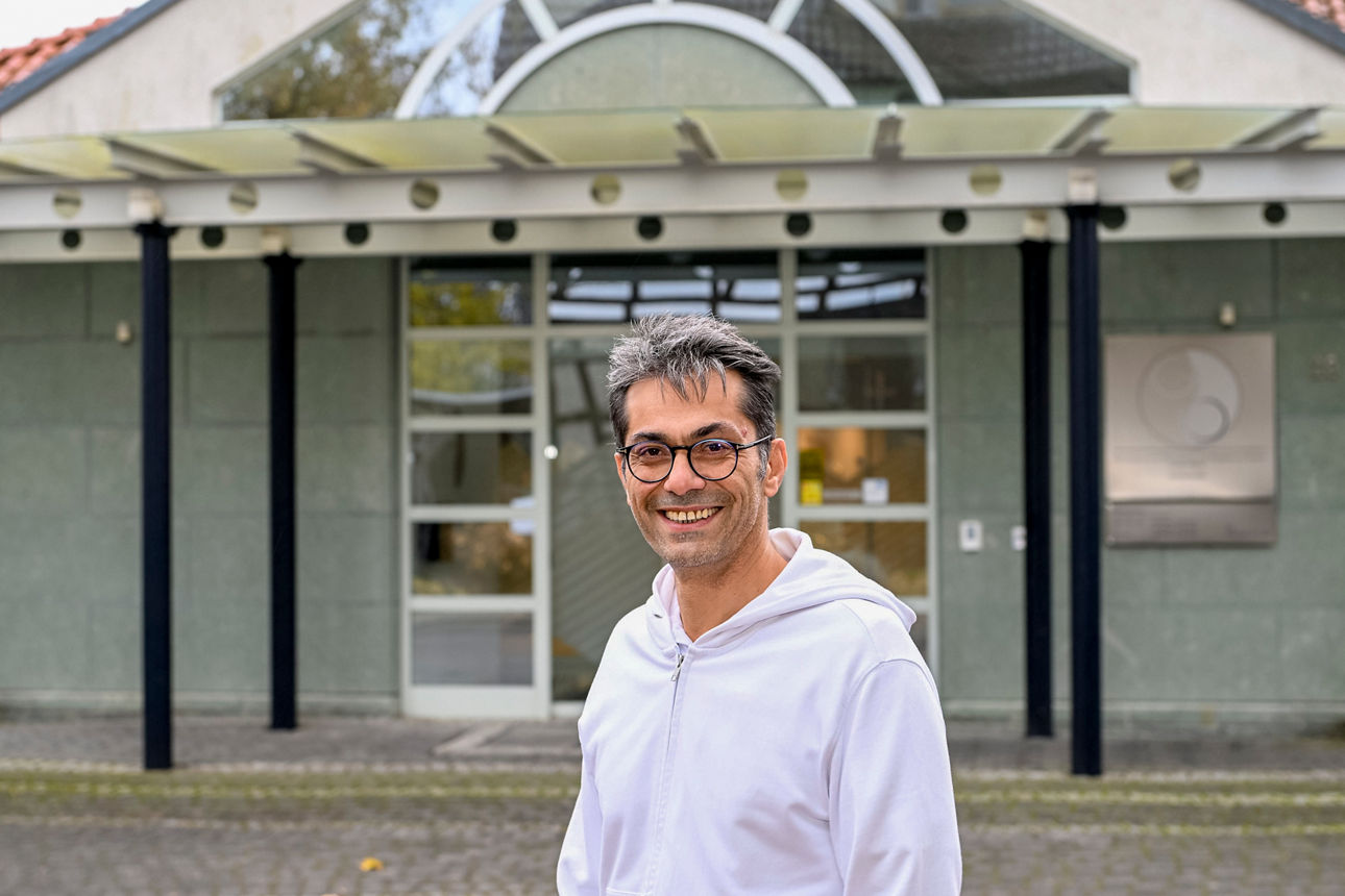 Dr. Gürdal Özkes steht vor seinem Praxisgebäude und lächelt in die Kamera