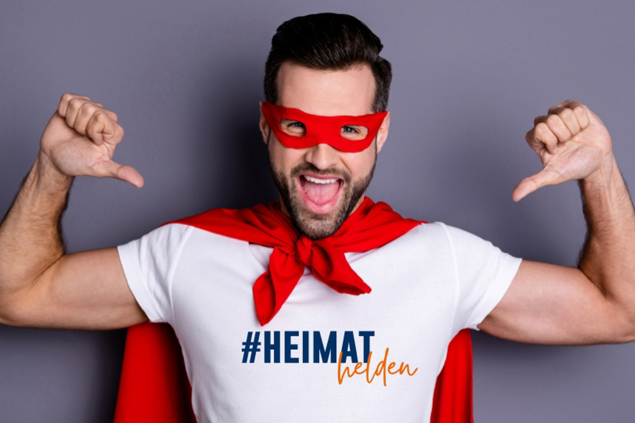 Junger Mannim Superhelden-Kostüm zeigt mit beiden Daumen auf sich selbst.