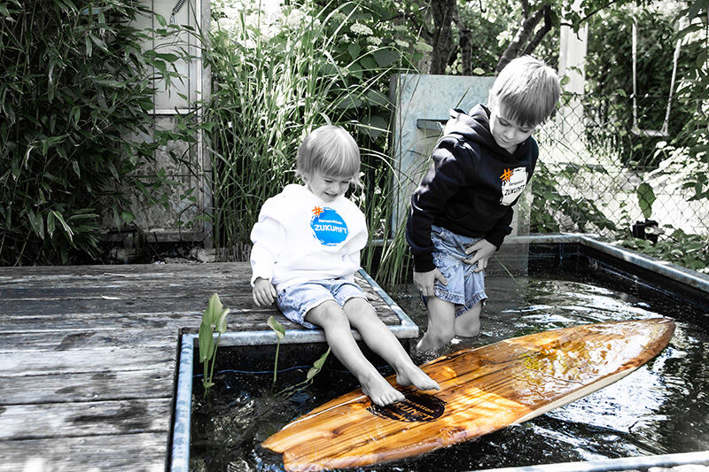 Kinder spielen am Wasser mit einem Surfbrett aus Holz