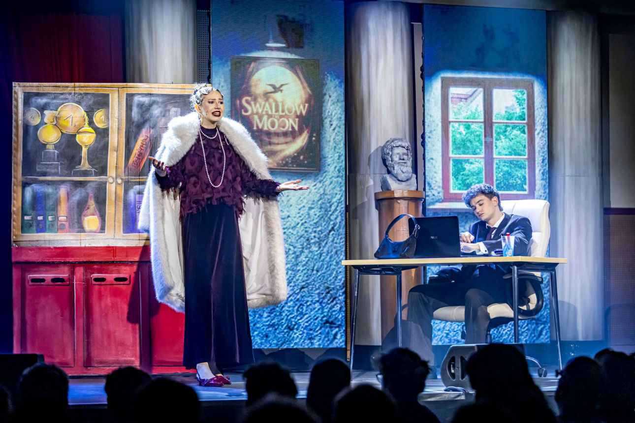 Broadway-Diva in festlicher Kleidung mit Schulleiter in Anzug hinter dem Schreibtisch