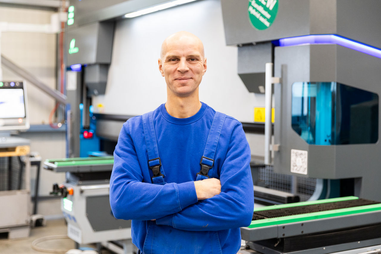 Sebastian Herrlich befindet sich im Produktionsbereich der „Herrlich GmbH“ vor einer modernen Abkantpresse. Die Aufnahme zeigt die Metallbearbeitungsanlage im laufenden Fertigungsumfeld mit Fokus auf präzise Blechbearbeitung und industrielle Produktionstechnik