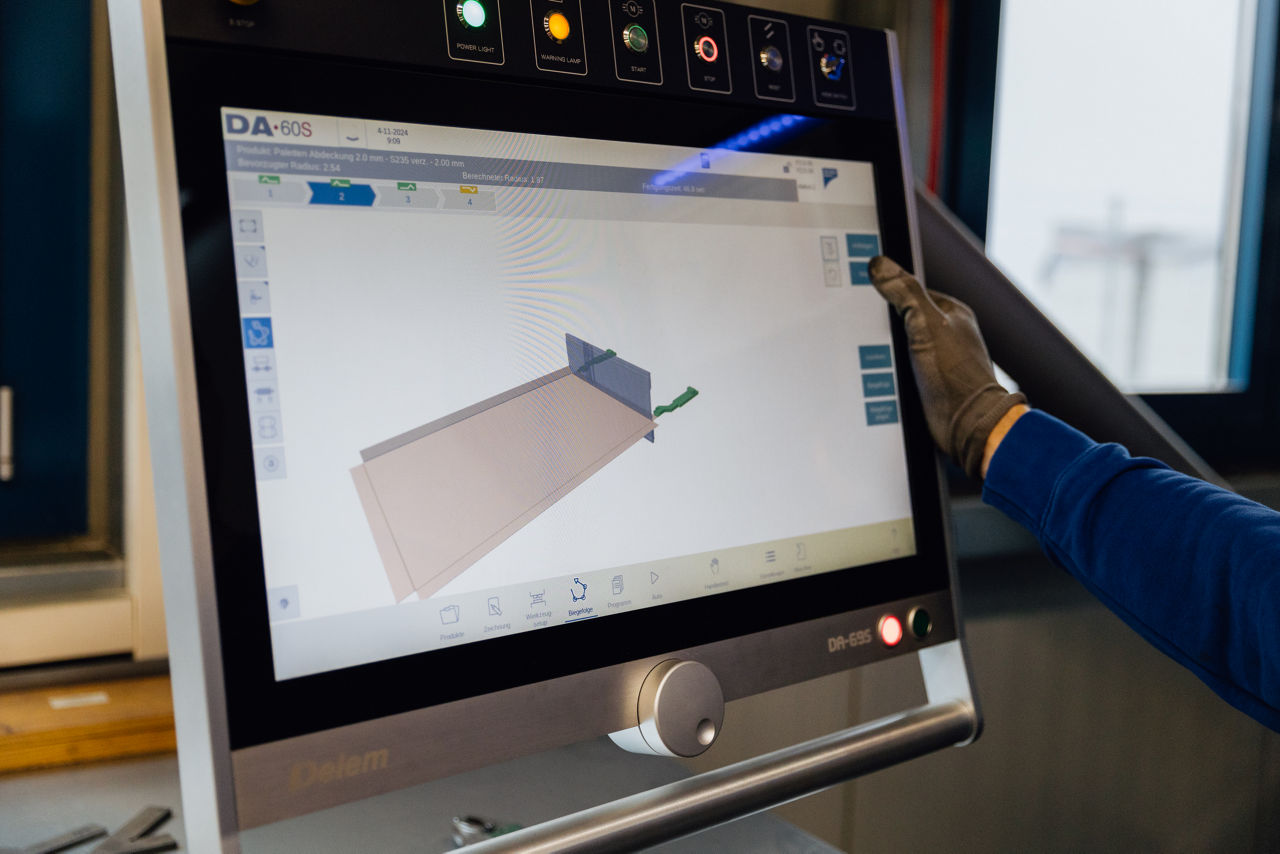 Bedienpanel einer CNC‑Maschine bei der „Herrlich GmbH“ mit grafischer Darstellung eines anstehenden Biegeprozesses. Sichtbar sind die digitalen Steuerungs‑ und Anzeigeelemente zur Vorbereitung und Kontrolle der Blechbearbeitung im Produktionsumfeld