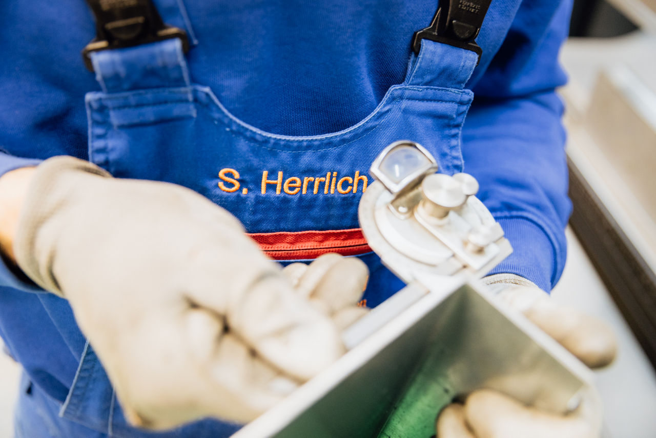 Detailaufnahme eines Messvorgangs an einem Metallbauteil bei der „Herrlich GmbH“ im Rahmen der Qualitätskontrolle. Sichtbar sind Messgerät und Werkstück, die zur Prüfung von Maßhaltigkeit und Fertigungsqualität im Produktionsprozess eingesetzt werden