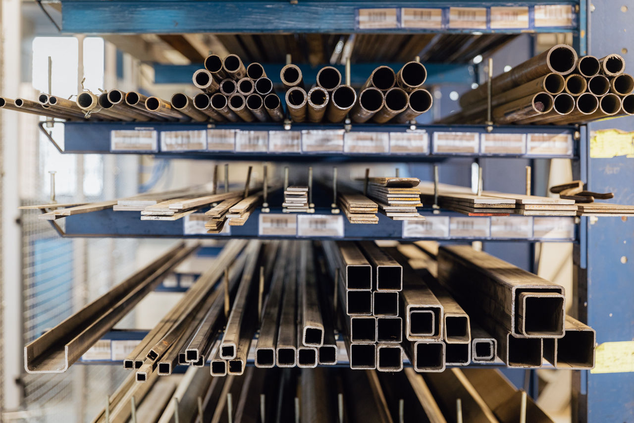 Lagerregal im Produktionsbereich der „Herrlich GmbH“ mit verschiedenen Metallprofilen und Rohren, die geordnet gelagert und für die Weiterverarbeitung im Rahmen der Metallbearbeitung vorbereitet sind