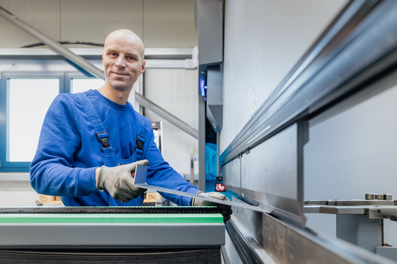 Bedienung einer CNC‑Abkantpresse bei der „Herrlich GmbH“ während des Abkantvorgangs eines Blechteils. Die Aufnahme zeigt den laufenden Fertigungsprozess mit Fokus auf präzise Blechbearbeitung und den Einsatz moderner CNC‑Technologie im Produktionsumfeld