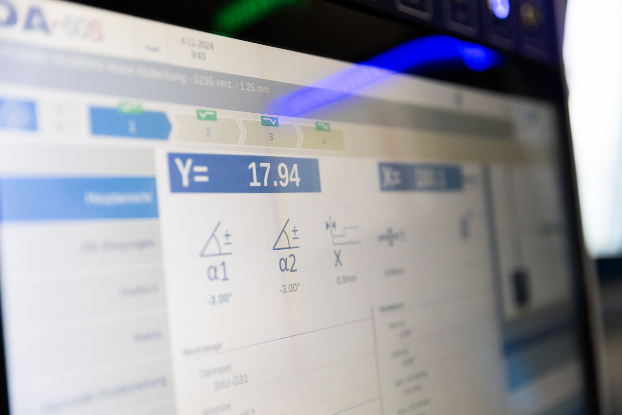 Steuerungsoberfläche einer CNC‑Abkantpresse bei der „Herrlich GmbH“ mit angezeigten Biegewinkeln und Prozessparametern für die Blechbearbeitung. Die Darstellung zeigt die digitale Bedienoberfläche zur Einstellung und Kontrolle des laufenden Abkantprozesses im Produktionsumfeld