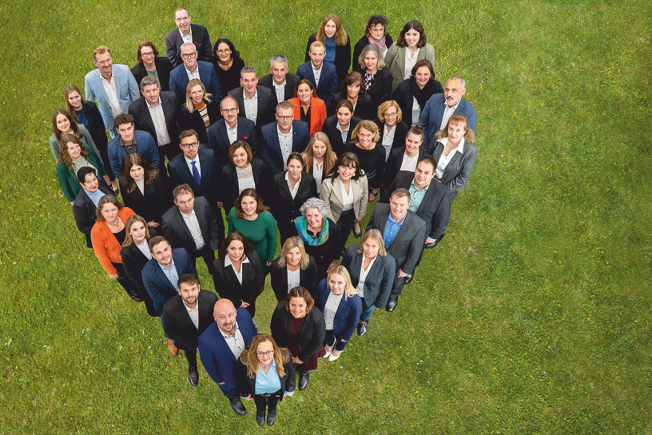 Mitarbeiter stehen in Herzform auf einer Wiese