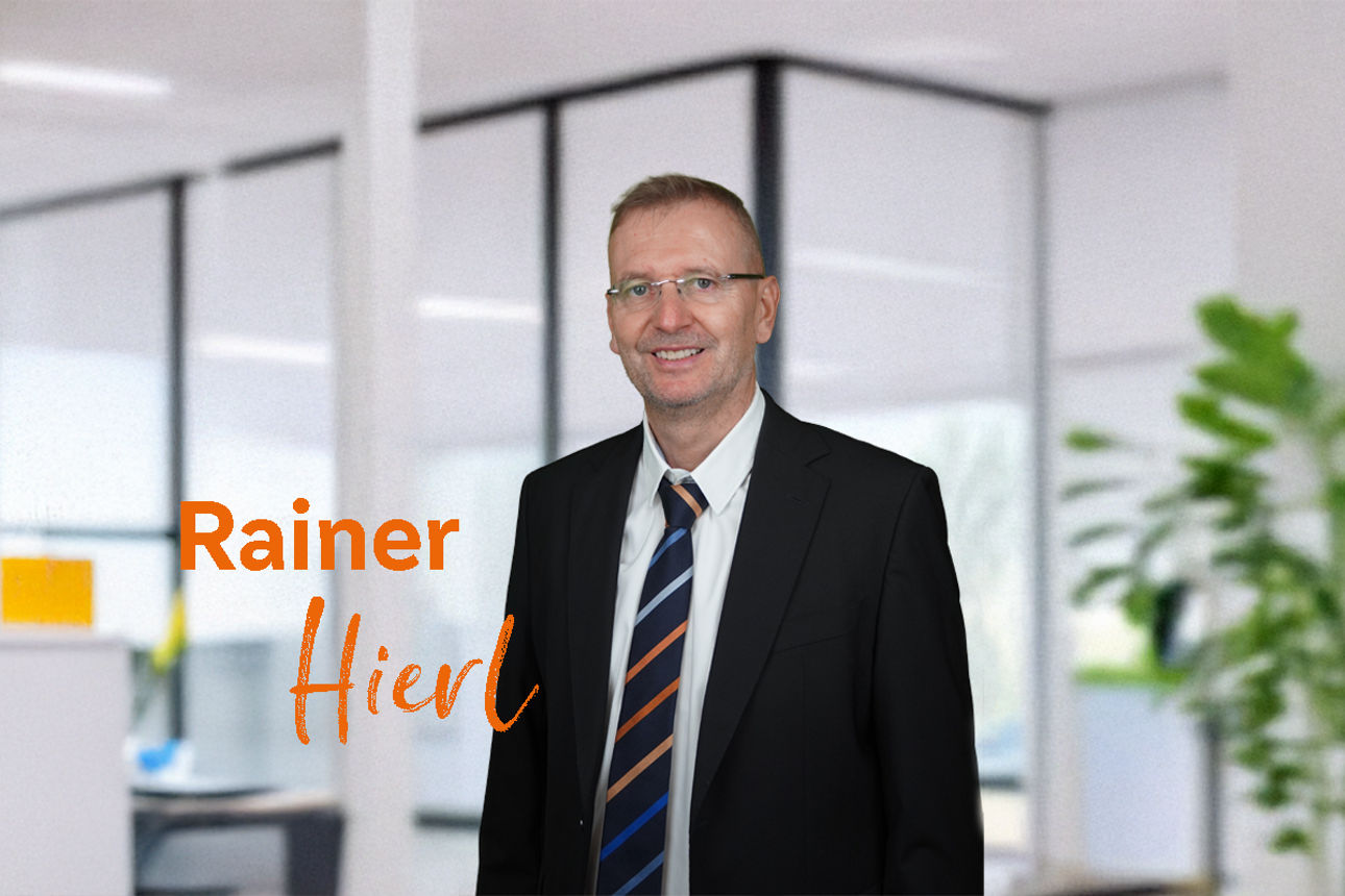 Das Bild zeigt einen Mann in einem Büro mit einem orangen Text "Rainer Hirl"