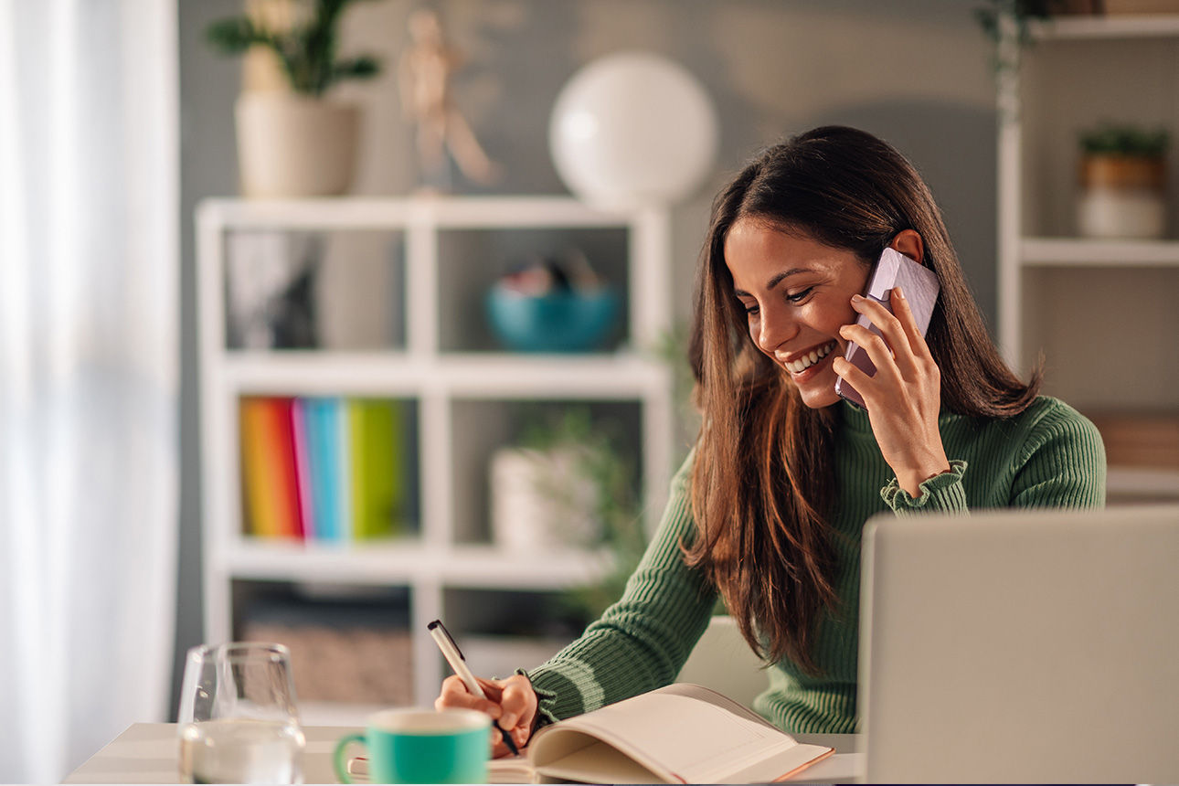 Frau am Telefon mit Laptop und Notizbuch