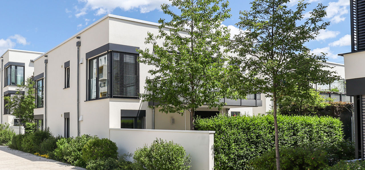 Modernes weißes Wohnhaus mit Flachdach, umgeben von Bäumen und Hecken