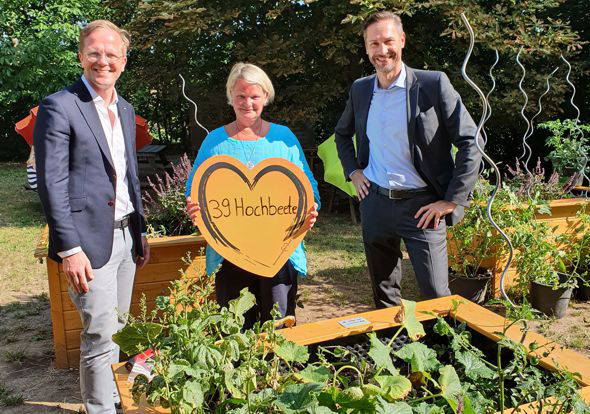 Drei Personen stehen in einem Garten, umgeben von üppigem Grün.