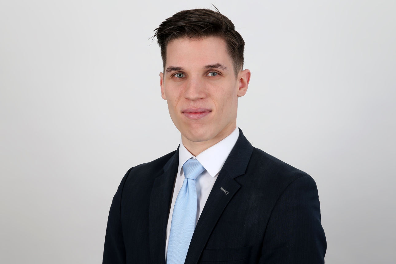 Ein lächelnder Mann in einem Anzug schaut in die Kamera.