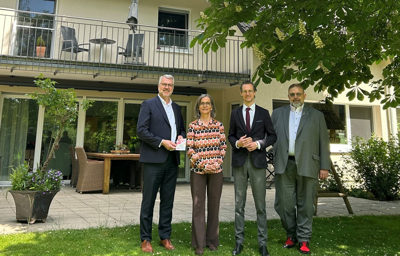 Klaus Dabbelt und Michael Burchard mit Mitarbeitern des Hospiz lebensHaus vor dem Gebäude unter einem grün blühenden Baum. 