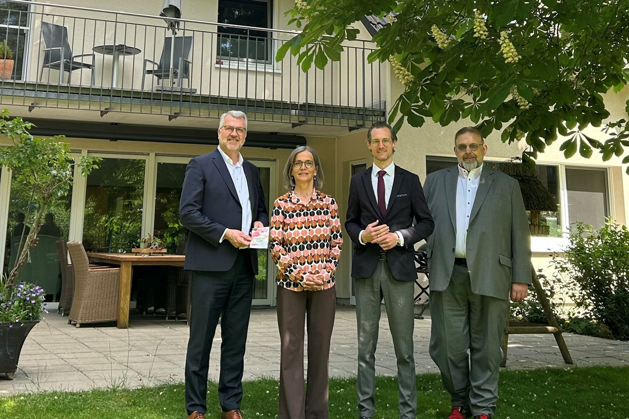 Klaus Dabbelt und Michael Burchard mit Mitarbeitern des Hospiz lebensHaus vor dem Gebäude unter einem grün blühenden Baum. 