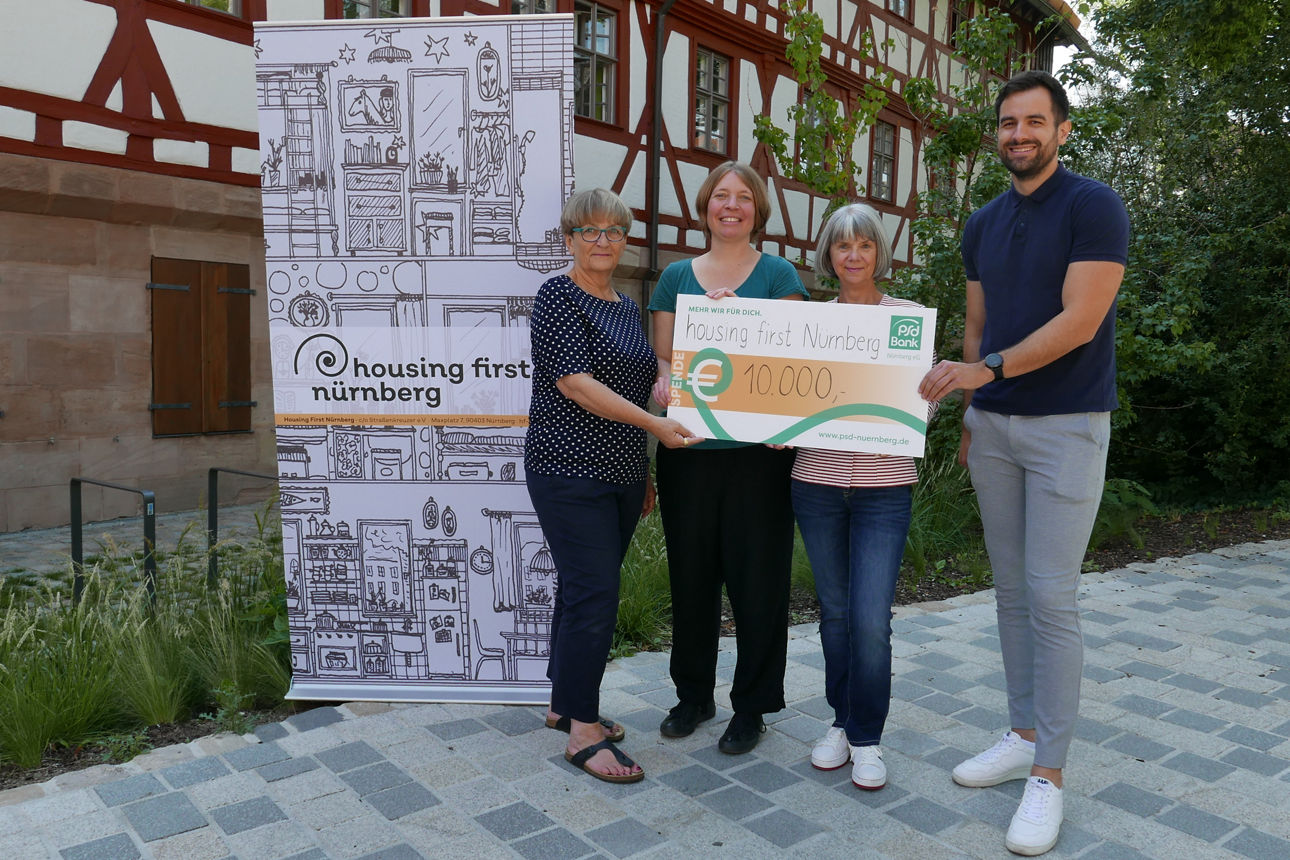 Ein Kollege der PSD Bank Nürnberg übergibt einen Spendencheck an housing first Nürnberg