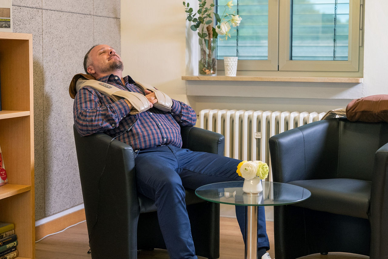 Ein Mann sitzt auf einem Stuhl und hat ein Massagegerät angelegt