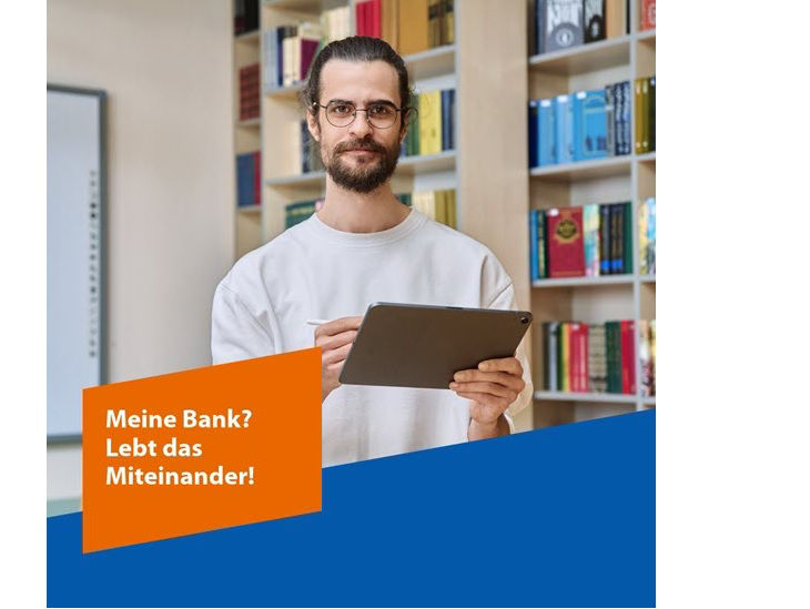 Ein junger Mann mit Zopf und Vollbart steht vor einem Bücherregal; dazu der Text: „Meine Bank? Lebt das Miteinander!“