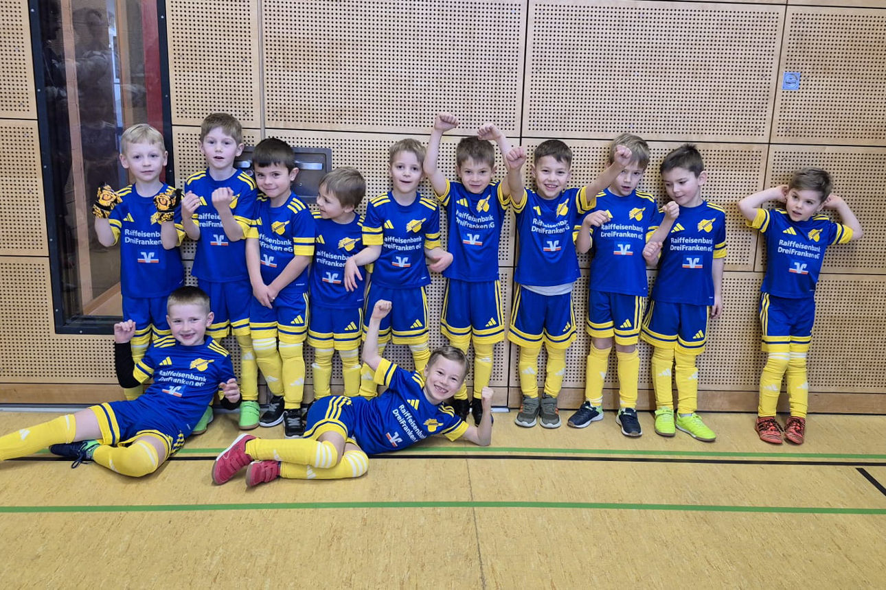 Junge Fußballer feiern die neuen Trikots in einer Sporthalle