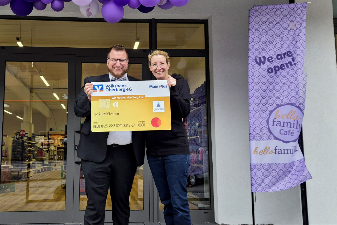 Ein Mann und eine Frau lächeln in die Kamera und halten gemeinsam eine übergroße, symbolische Bankkarte der Volksbank Oberberg.