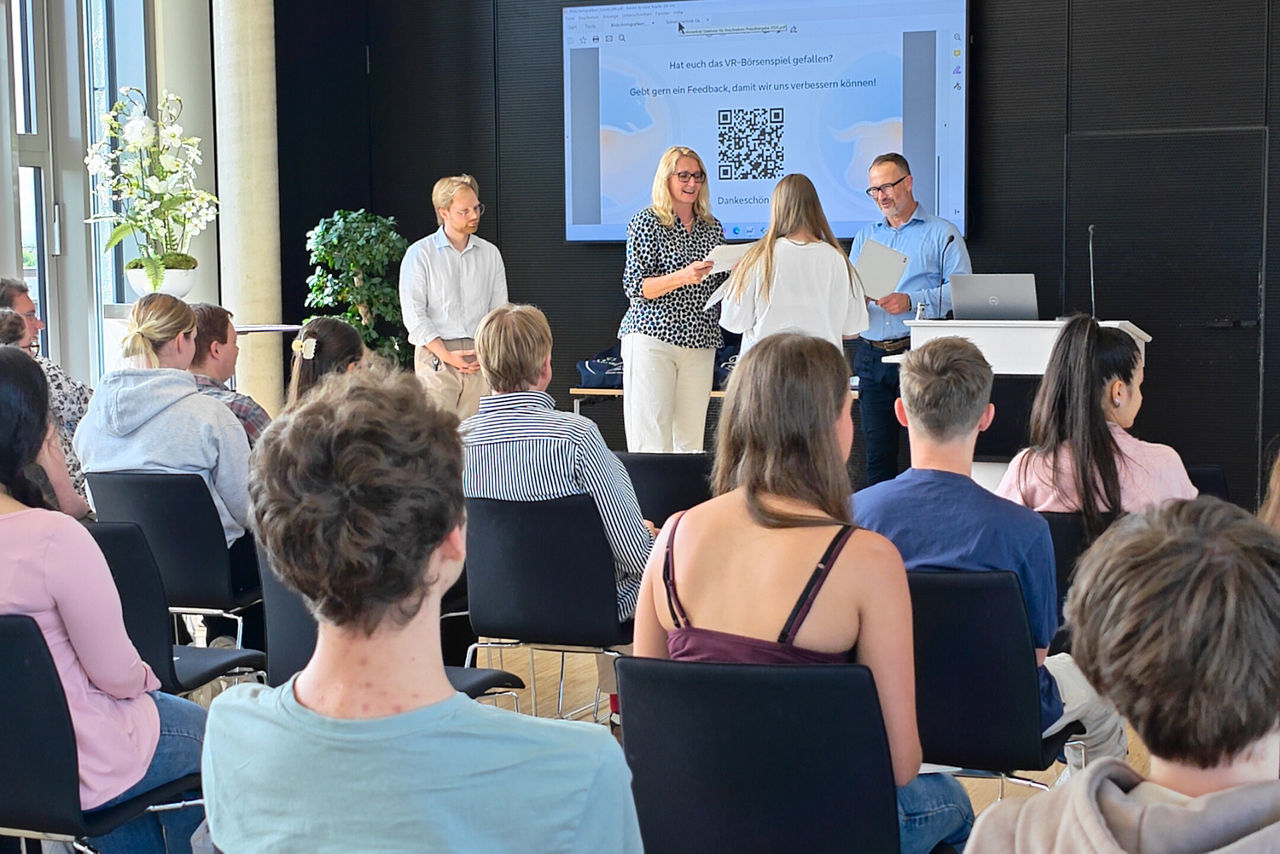 Gesamtaufnahme im Forum der Volksbank Ruhr Mitte, während der Preisverlehung zum VR-Börsenspiel 2026 mit der Gesamtschule Erle aus Gelsenkirchen. Vorne am rednerpult steht Christoph Osigus (Leiter FinanzCenter Gelsenkirchen-Buer), mit Daniela Klüsener und Thorben Schiewe von der Volksbank  und Übergibt die Urkunden. 