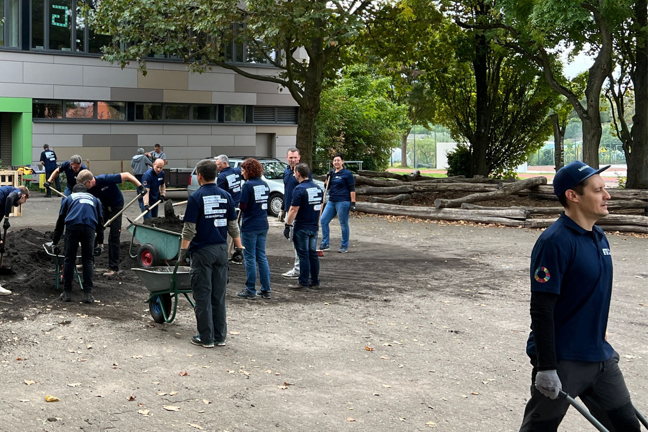 Menschen stehen auf einem Schulhof und erneuern das Gelände.