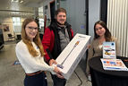 Zwei Frauen überreichen einem Mann ein Paket