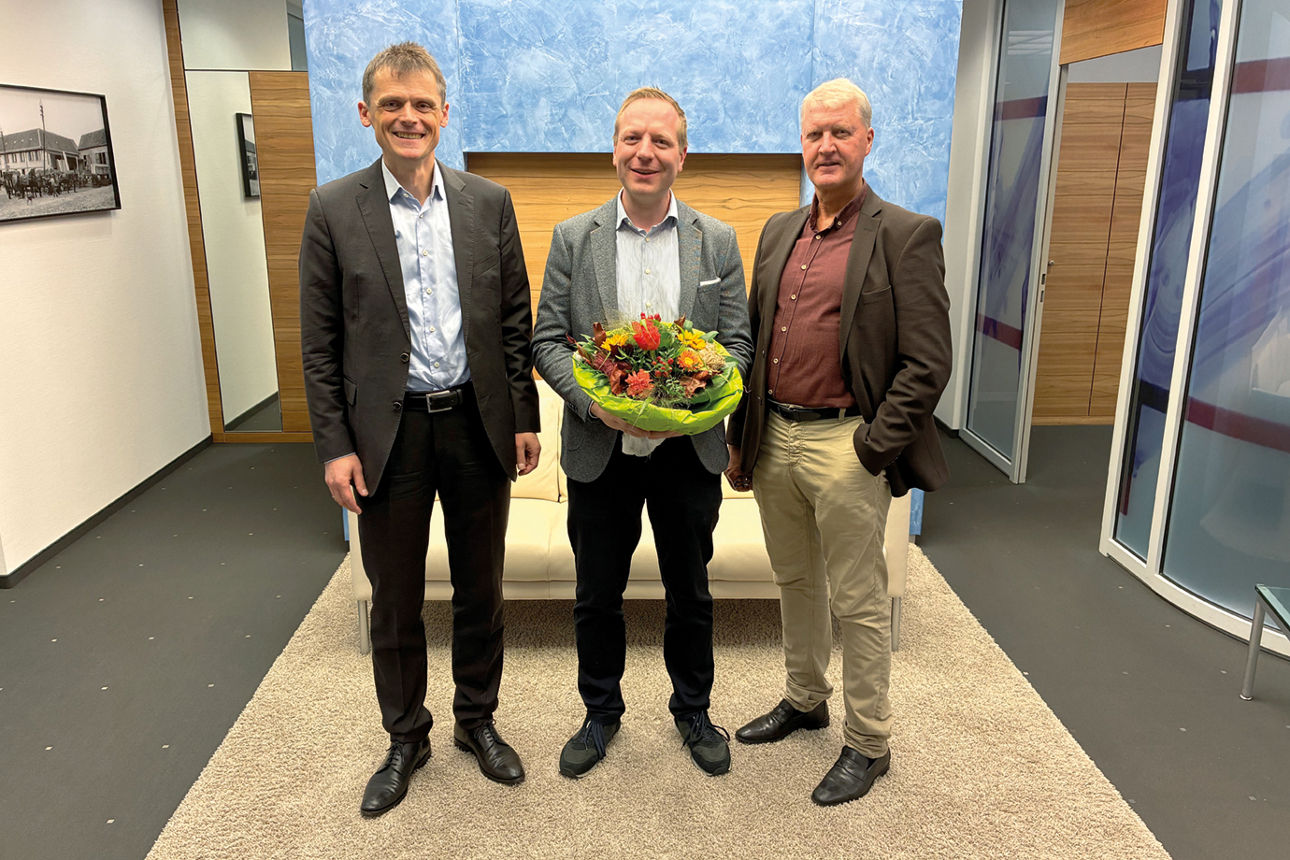 Jan Peter Karl hält einen Blumenstrauß. Helmut Vilmar und Christoph Gubert stehen neben ihm.