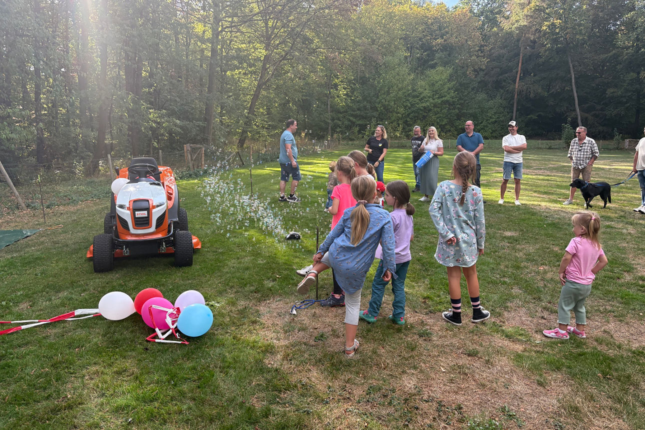Kinder stehen vor einem neu enthüllten Rasenmähertraktor auf dem Sportplatz.