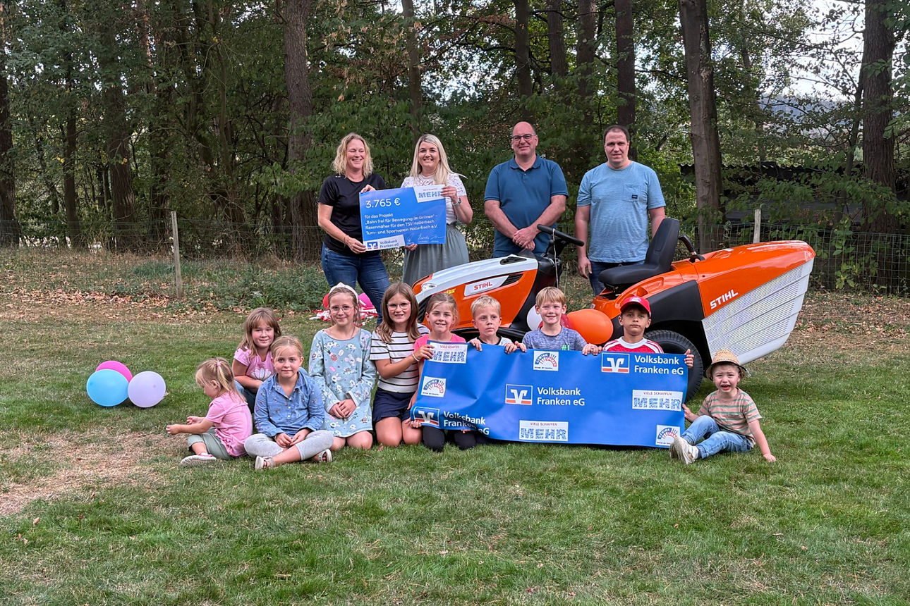 Gruppenfoto mit Spendenscheck und neuem orangefarbenen Rasenmähertraktor beim TSV Hollerbach.