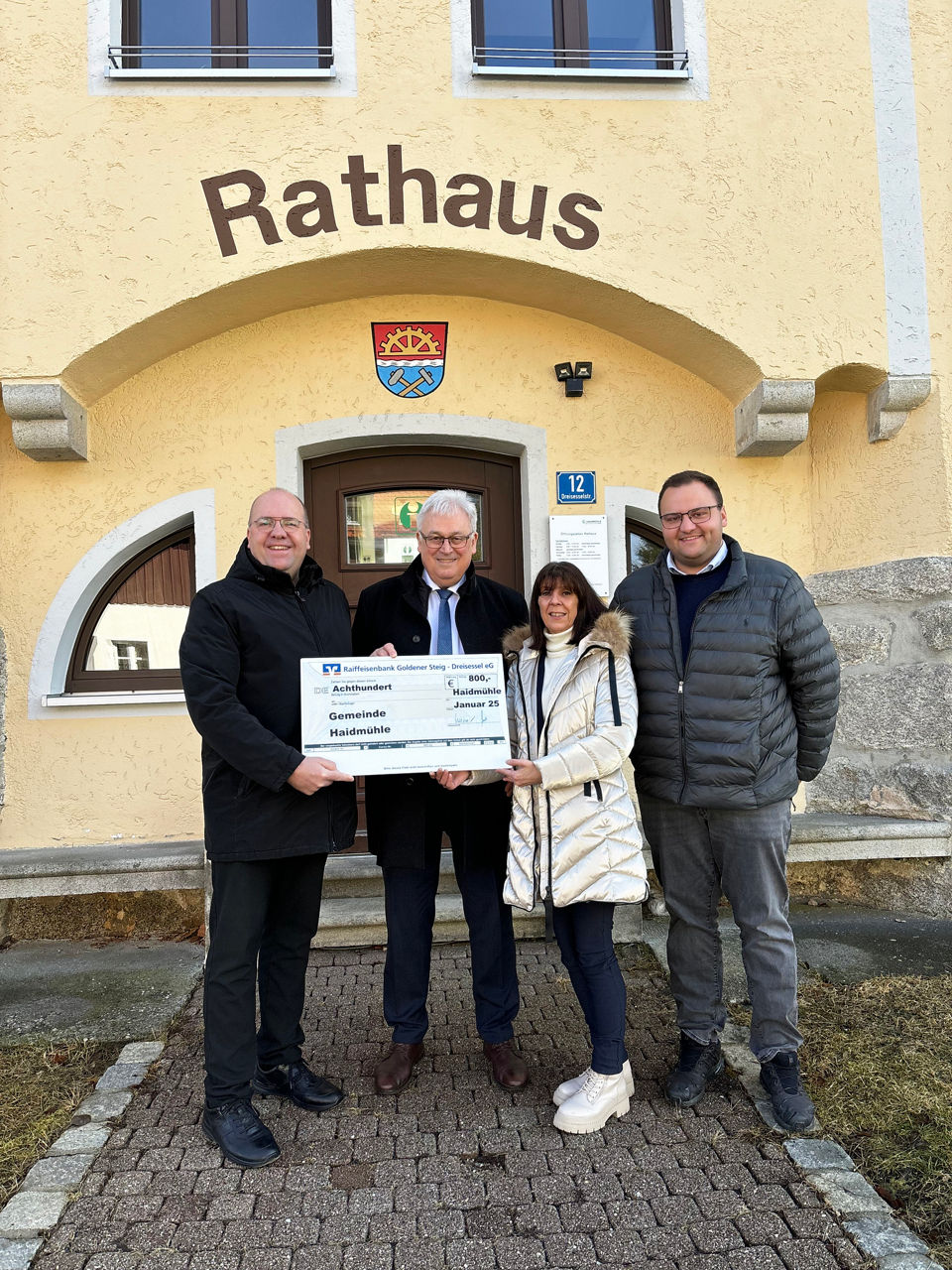 drei Männer und eine kleine Frau stehen vor dem Haidmühler Rathaus und halten einen Scheck