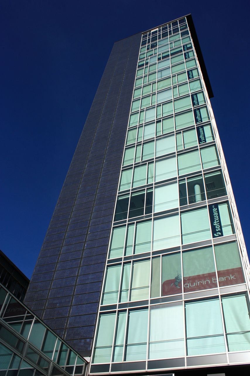Auf dem Bild ist ein großes gläsernes Gebäude  zu sehen. Im Hintergrund ist ein klarer blauer Himmel zu sehen.