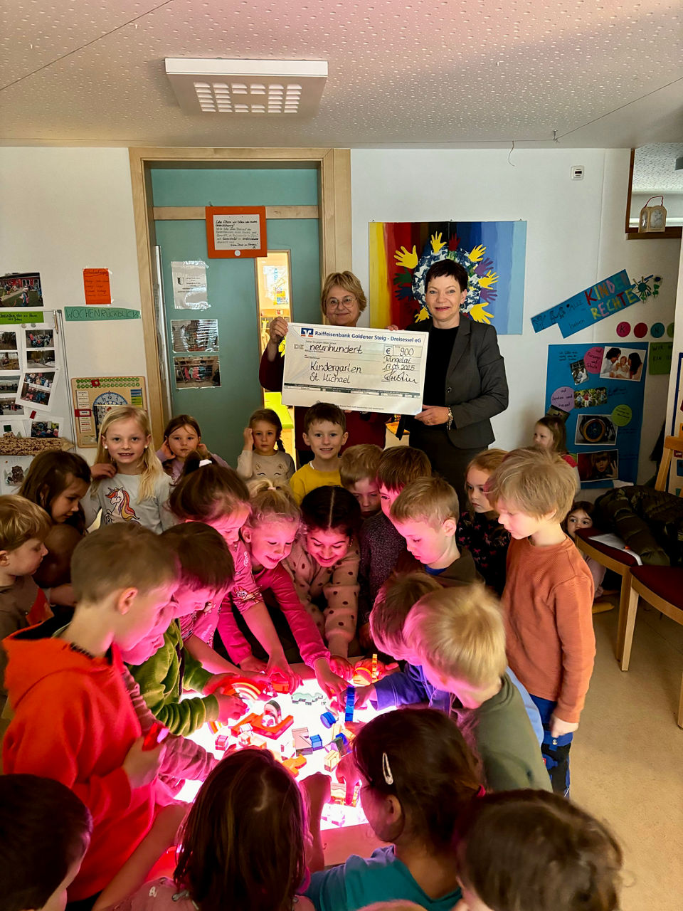 viele Kindergartenkinder versammelt um einen Leuchttisch, zwei Damen im Hintergrund