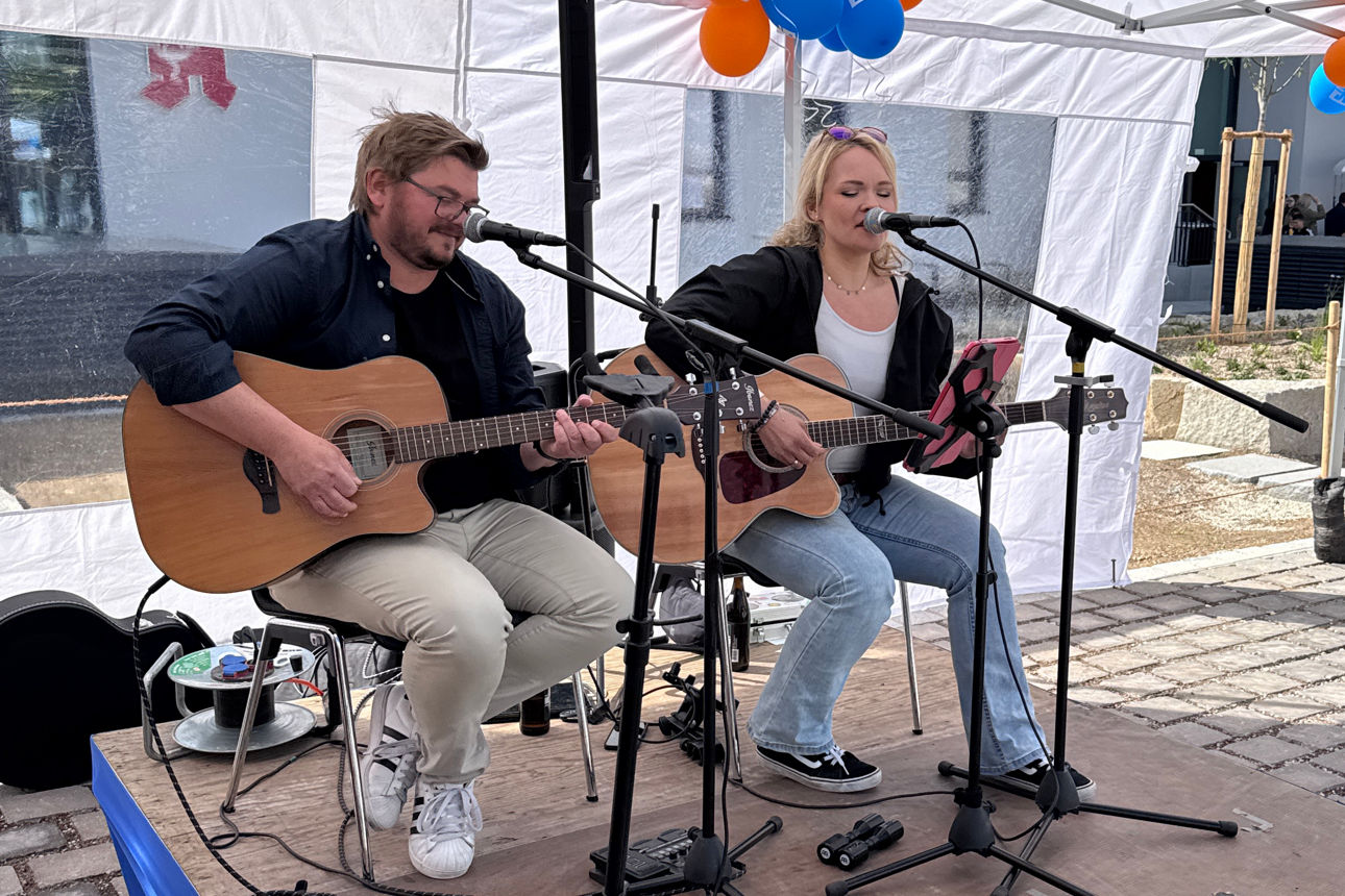 Zwei Personen mit Gitarre und Mikrofon auf Bühne beim musizieren
