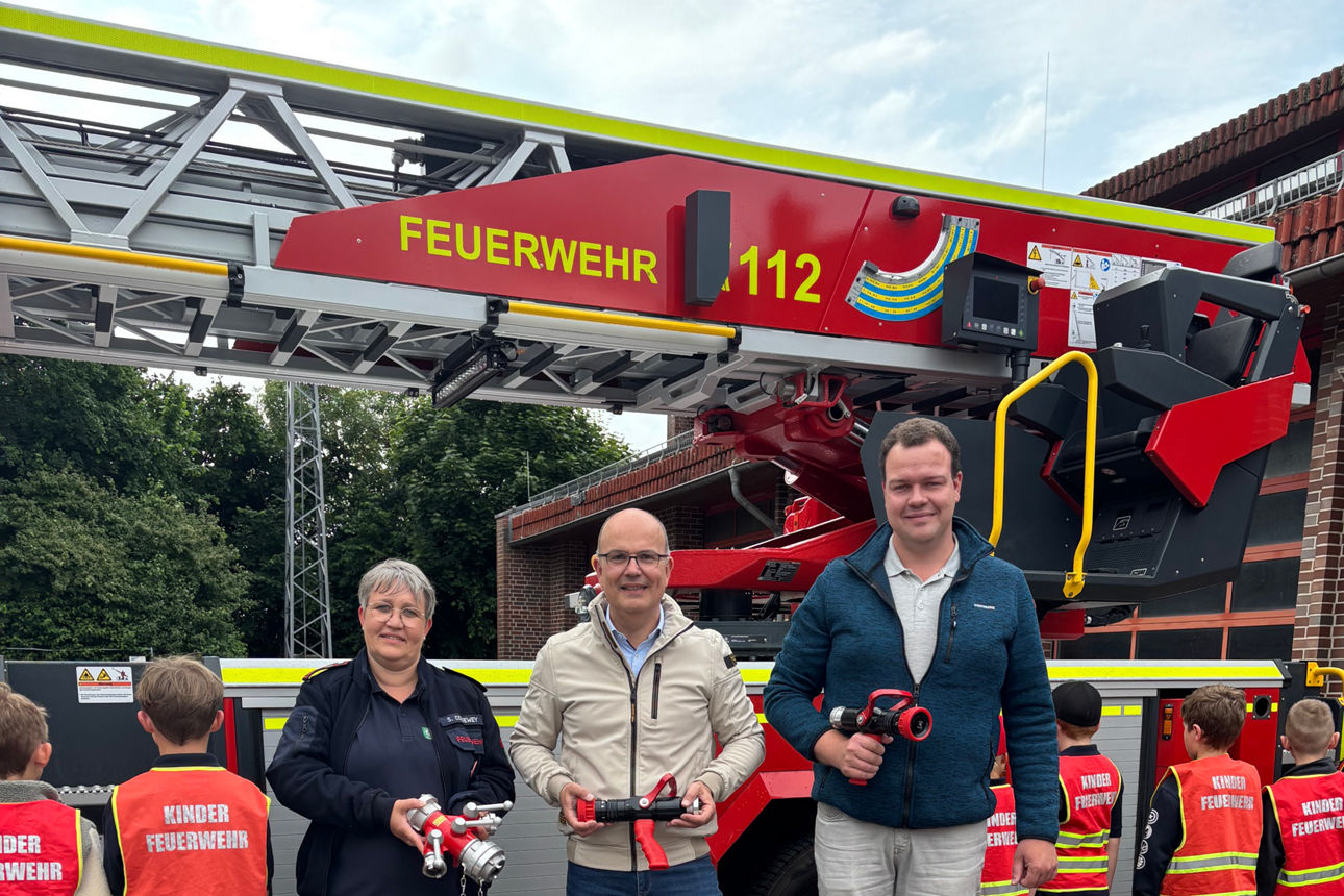 Drei Personen mit Sachspenden, im Hintergrund Kinder mit Warnwesten.