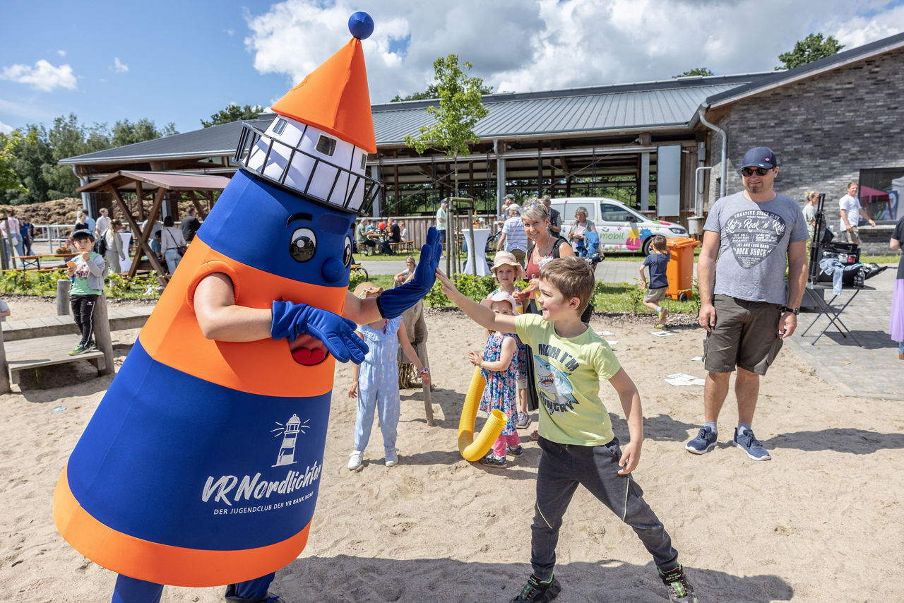 Ein Junge klatscht das Maskottchen der VR Bank Nord eG ab.