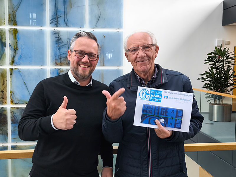 Zwei Männer lächeln und halten ein Schild mit einer Daumen-hoch-Geste.
