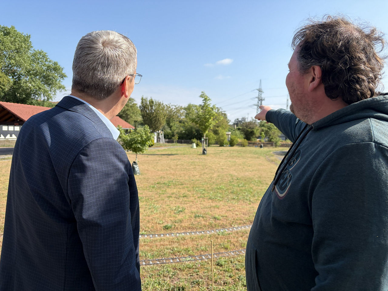 Zwei Männer stehen auf einen Feld und sehen sich den neugepflanzten Baum an