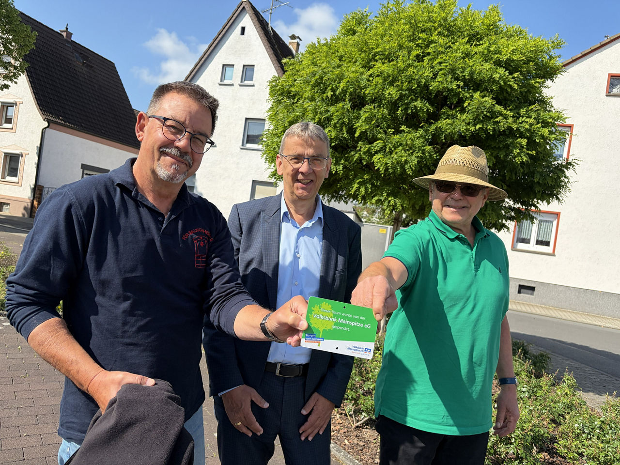 Drei Männer halten das neue Baumschild von der Volksbank Mainspitze in den Händen