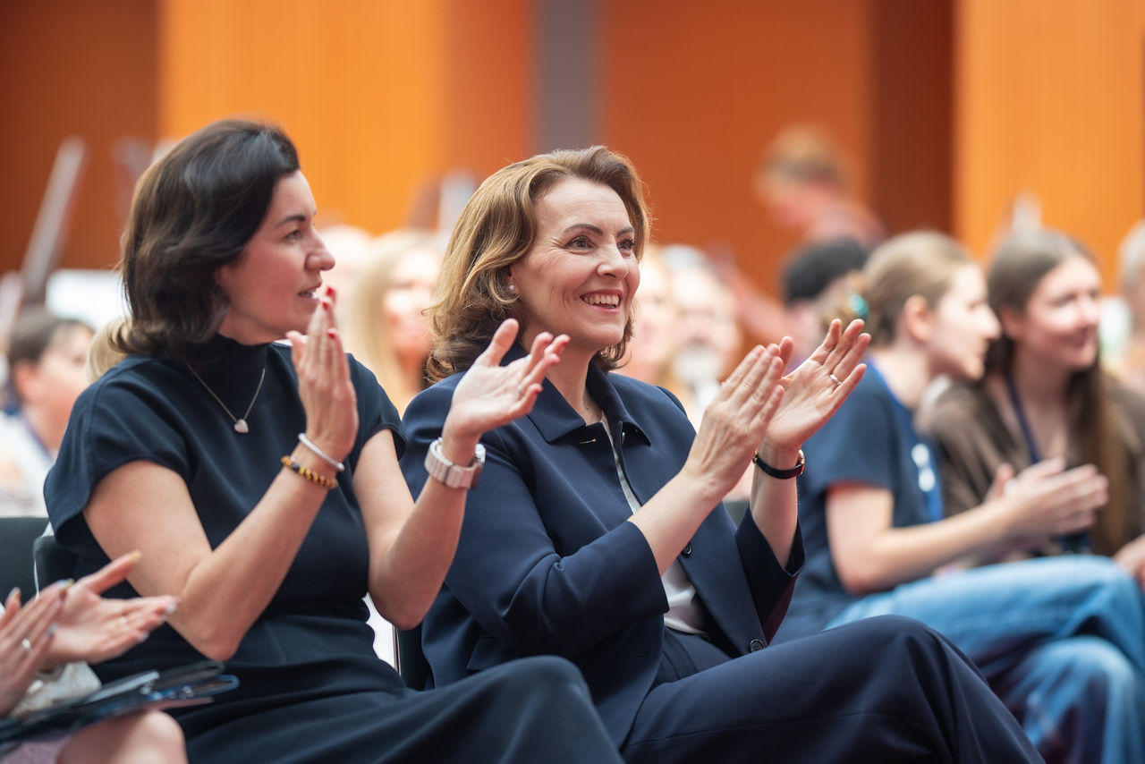 Zwei Frauen im Publikum in Business-Kleidung applaudieren und lächeln