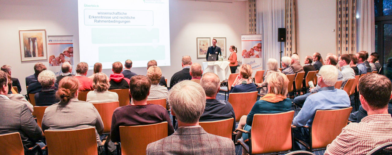 Eine große Gruppe von Menschen sitzt in einem Konferenzsaal und hört aufmerksam einem Vortrag zu.