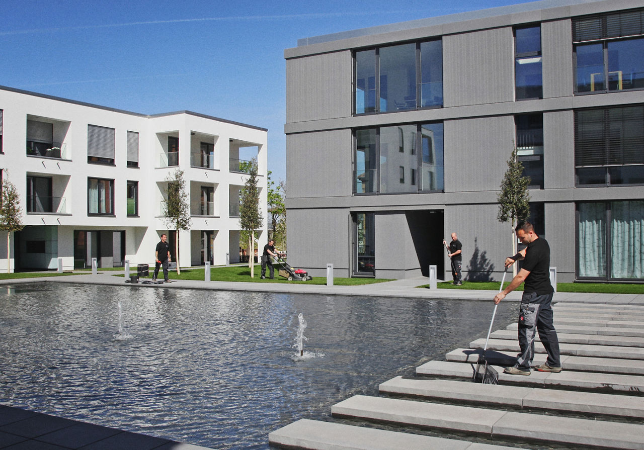 Vier Personen erledigen Reinigungs- und Gartenarbeit zwischen modernen Häuser und einem Wasserbecken