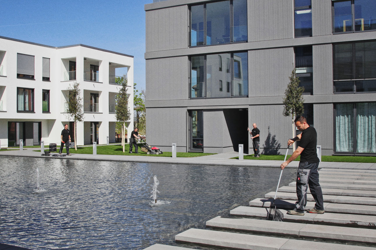 Vier Personen erledigen Reinigungs- und Gartenarbeit zwischen modernen Häuser und einem Wasserbecken