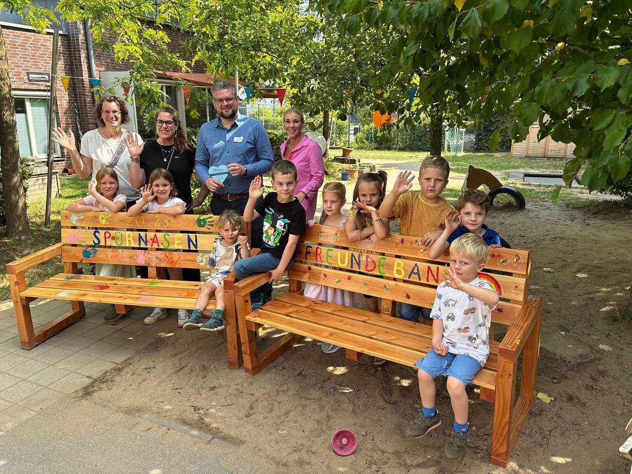 Kinder und Erwachsene stehen hinter den Bänken. 