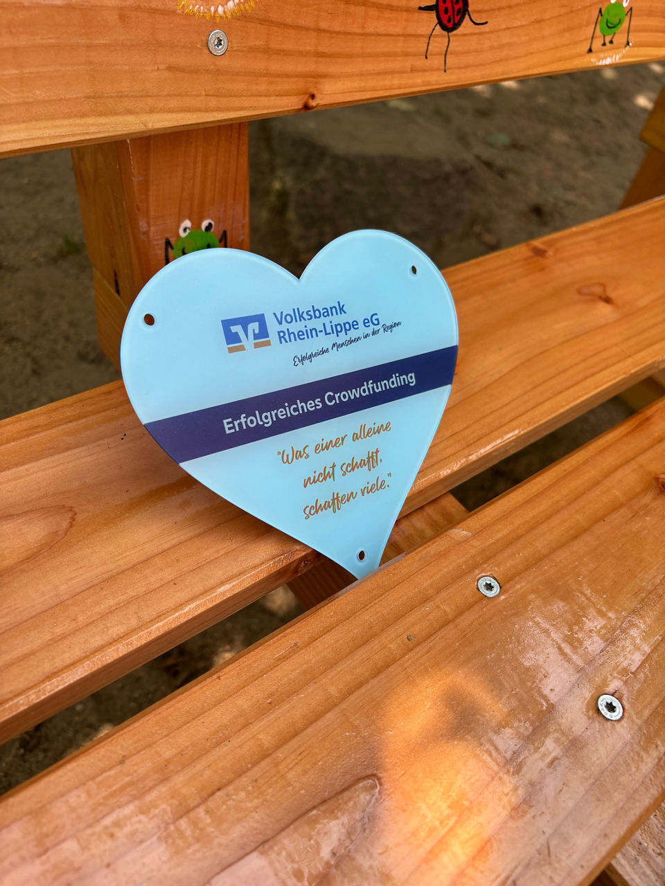 Ein Schild in Form eines Herzens mit dem Banknamen auf einer Holzbank.