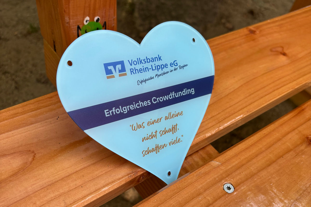 Ein Schild in Form eines Herzens mit dem Banknamen auf einer Holzbank.