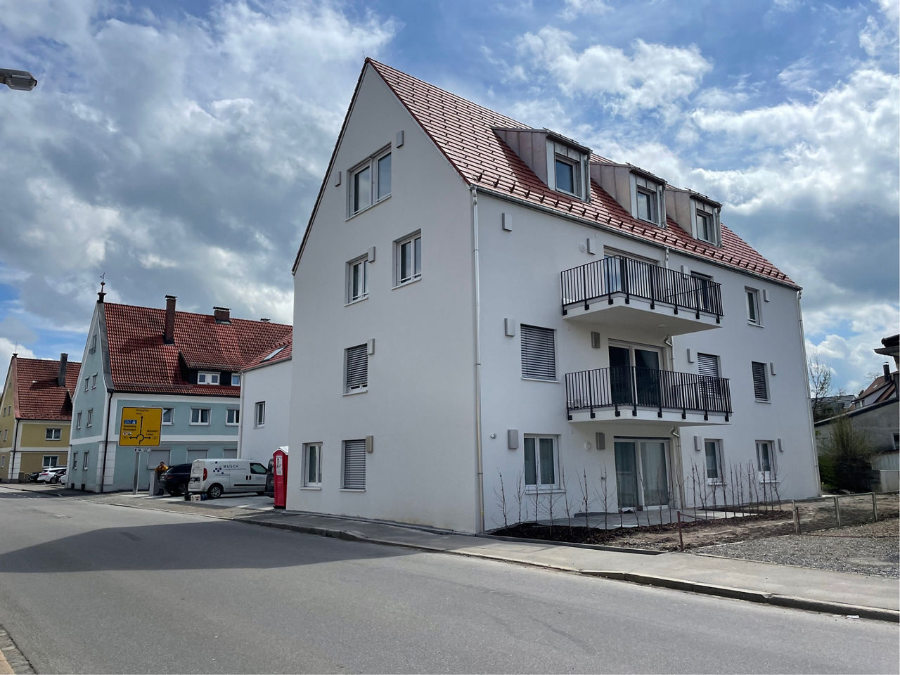 Weißes neues Mehrfamilienhaus mit Spitzdach in Wangen im Allgäu. Es sind Balkone zu sehen.