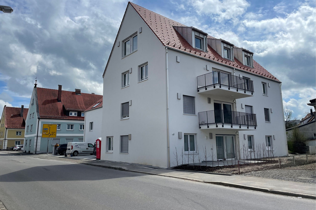 Weißes neues Mehrfamilienhaus mit Spitzdach in Wangen im Allgäu. Es sind Balkone zu sehen.