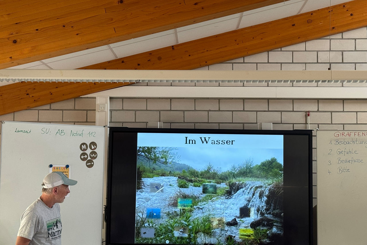 Ein Referent steht in einem Klassenraum neben einer Präsentation über Tiere und Pflanzen im Wasser.